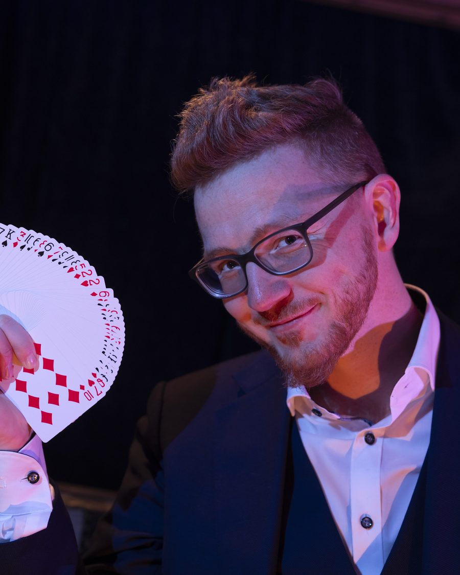 Magier Tino Plaz mit aufgefächerten Spielkarten, vor dunklem Hintergrund